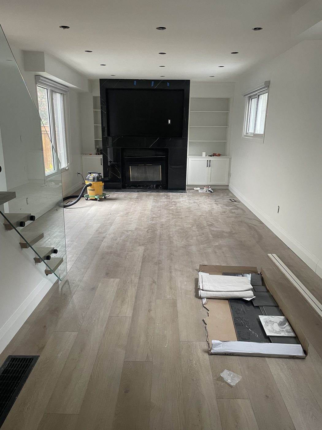Basement lounge with marble-clad fireplace, built-ins, and a glass stair railing.