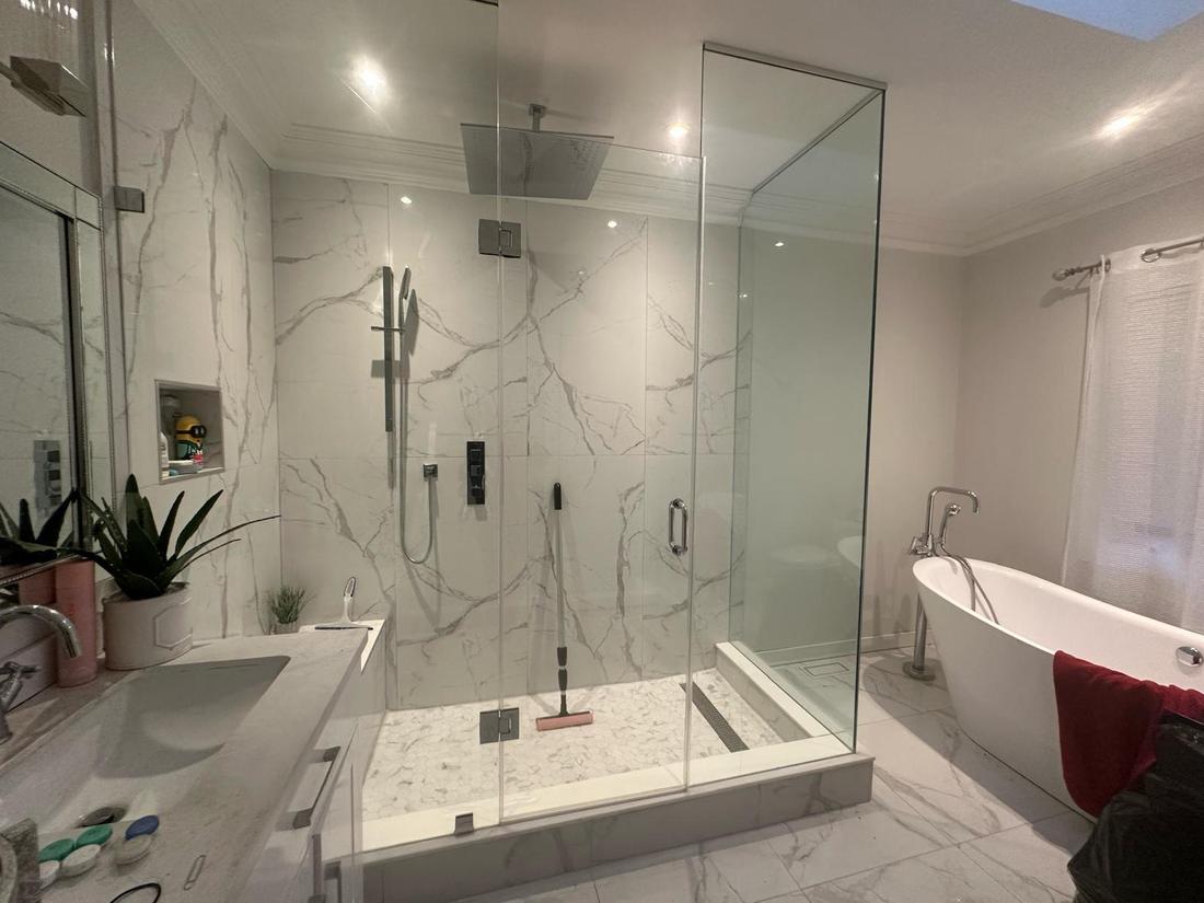 Custom walk-in shower with large-format marble-look tile, frameless glass, and rainfall fixtures.